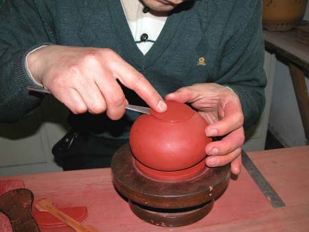 34、再次用“旁皮刀”挑挾起壺底片，塞填進壺底圈內，並用手靈巧的壓緊黏合處的圓周。