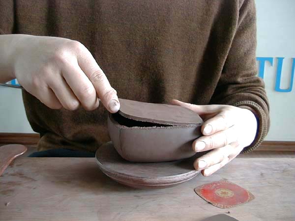 10、旁皮刀挑起壶底底片，小心的套黏入壶身筒内，至泥片平整，壶身不变型始可。
